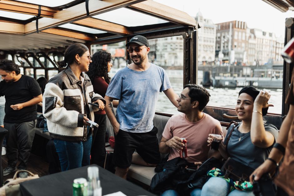 A group on a covered canal boat in Amsterdam, talking with drinks in hand