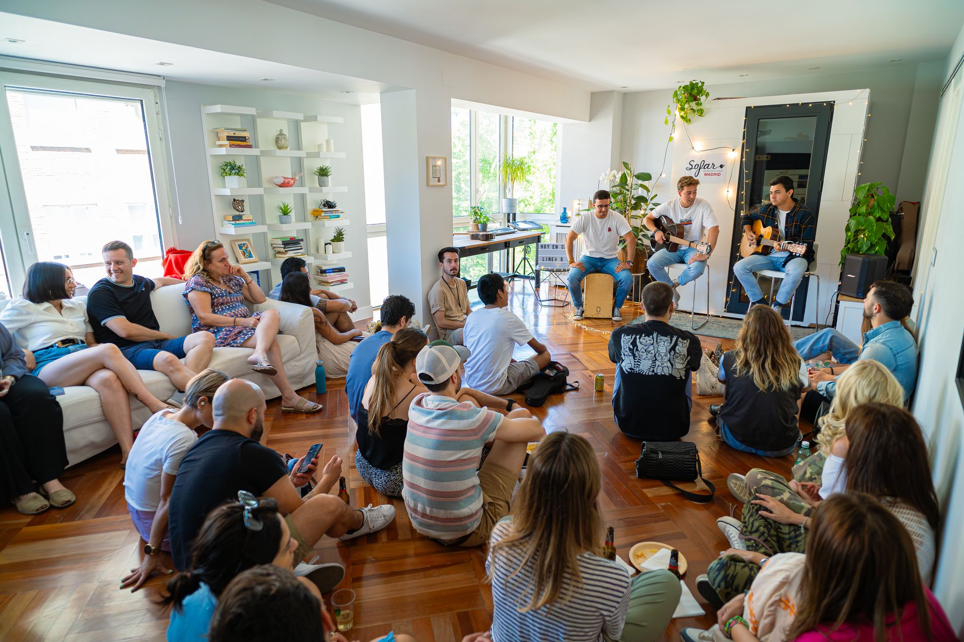 Musicians playing guitars to a small seated audience in a living room