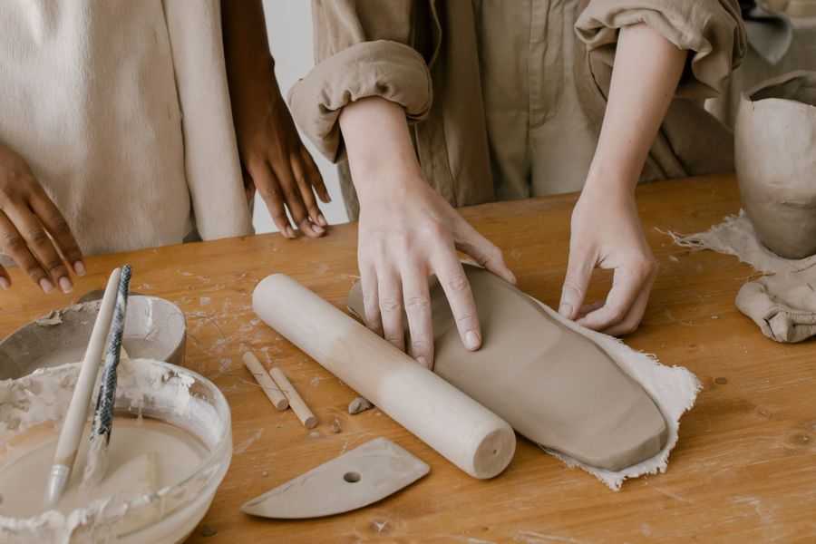 Several pairs of hands shaping clay at a workshop table