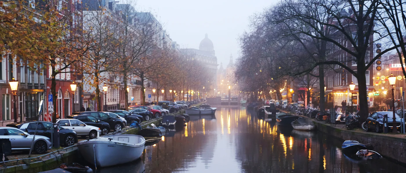 A quiet Amsterdam canal in daylight, boats moored along it