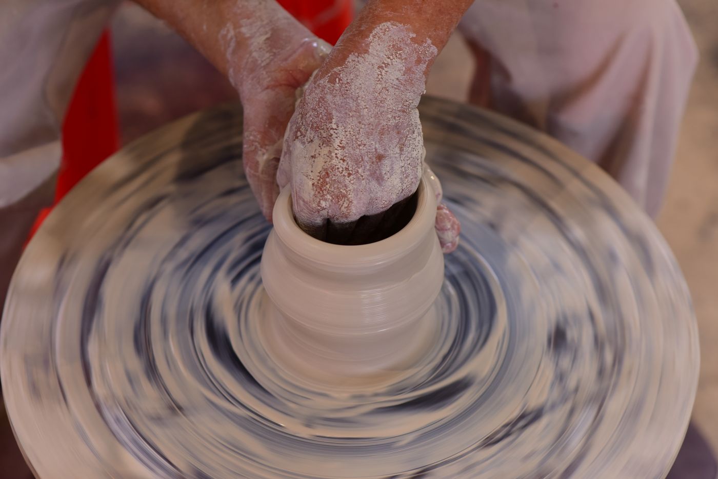 Hands shaping a pot on a spinning pottery wheel