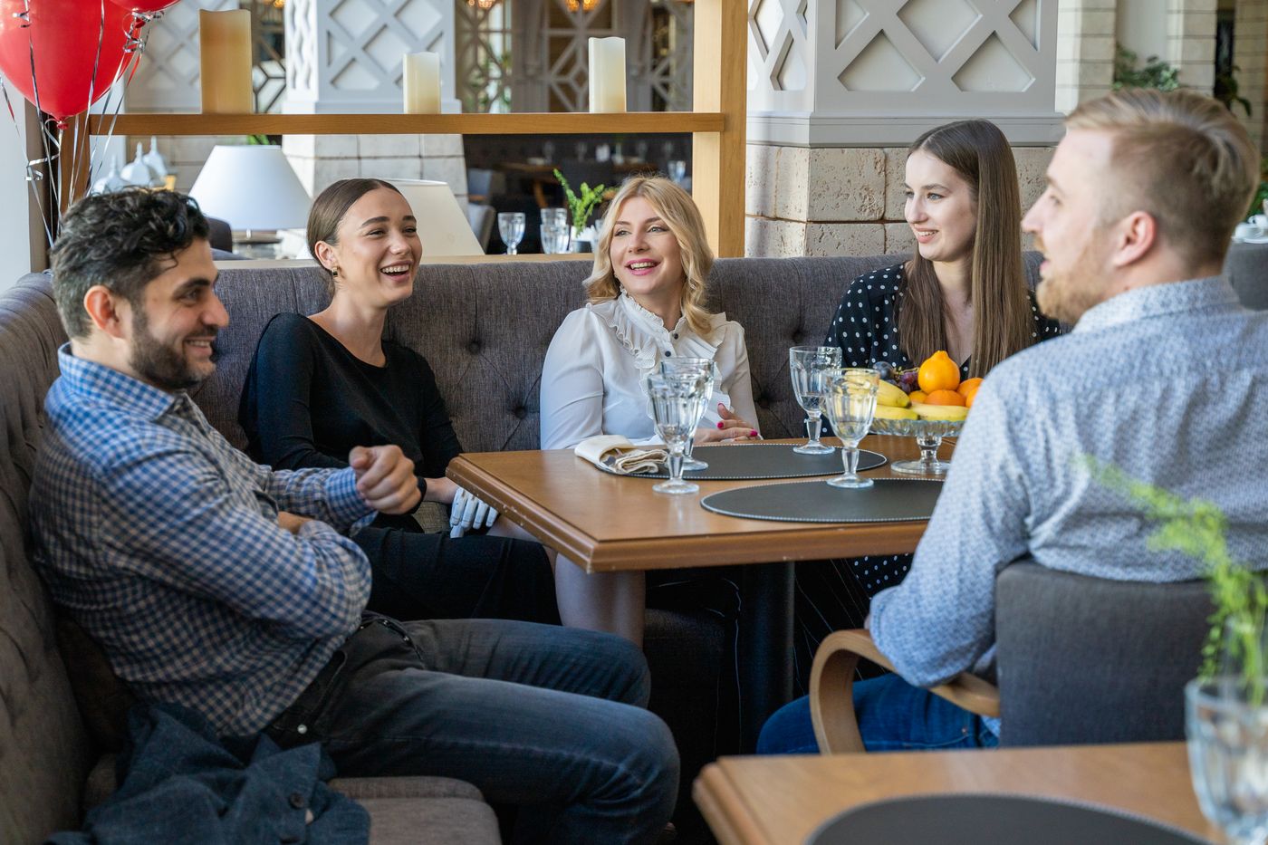 Five friends laughing together around a restaurant table