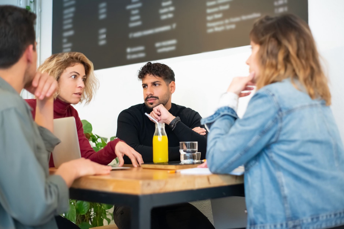 Four people in a discussion around a café table with a laptop
