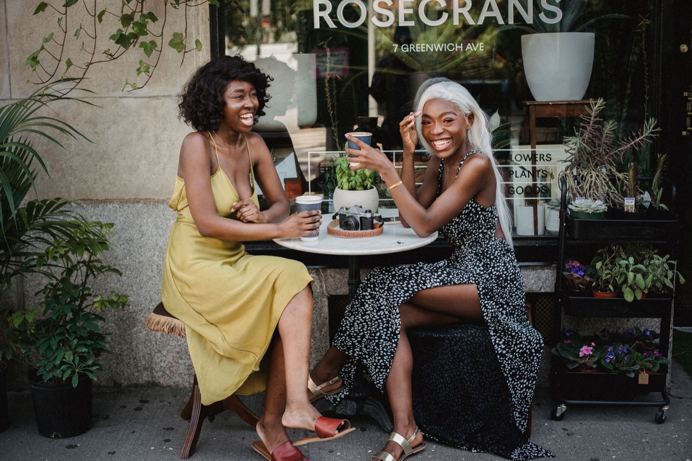 Two women laughing over coffee at a table outside a café