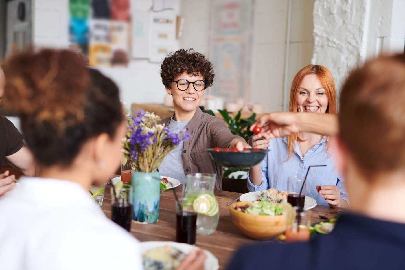 Friends passing a bowl across a wooden table at lunch