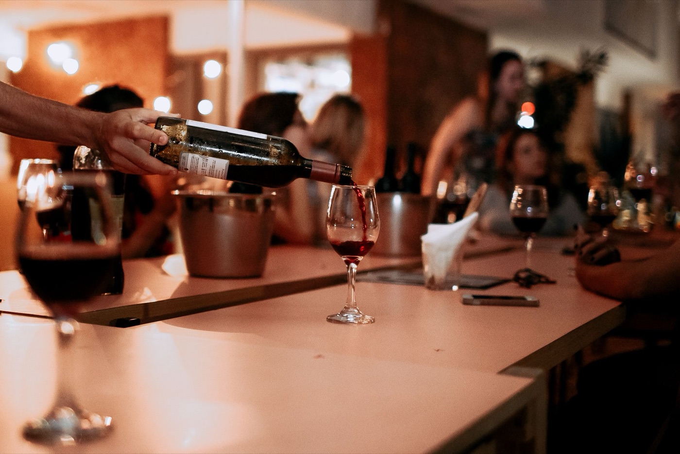 Wine being poured at a bar with people talking behind